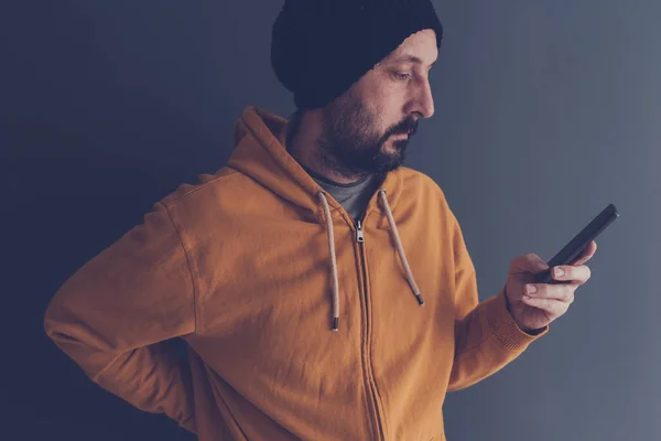 Casual adulto masculino com tampa olhando para o telefone móvel — Fotografia de Stock