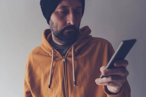 Maschio adulto casual con cappuccio guardando il telefono cellulare — Foto Stock