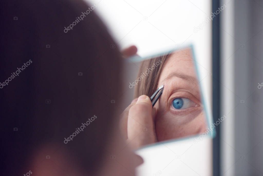 Woman plucking eyebrows by the window