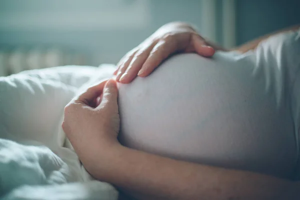 妊娠中の女性が自宅の寝室で腹を抱きしめる — ストック写真