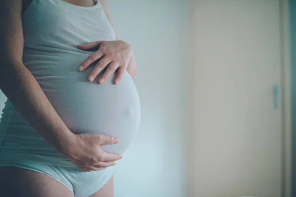 Беременная женщина обнимает живот в спальне дома — стоковое фото