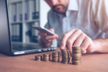 Ön planda yığılmış paralar ile Smartphone kullanarak iş adamı