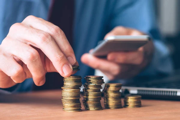 Empresario usando smartphone con monedas apiladas en primer plano — Foto de Stock