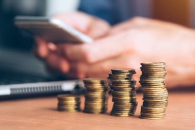 Ön planda yığılmış paralar ile Smartphone kullanarak iş adamı