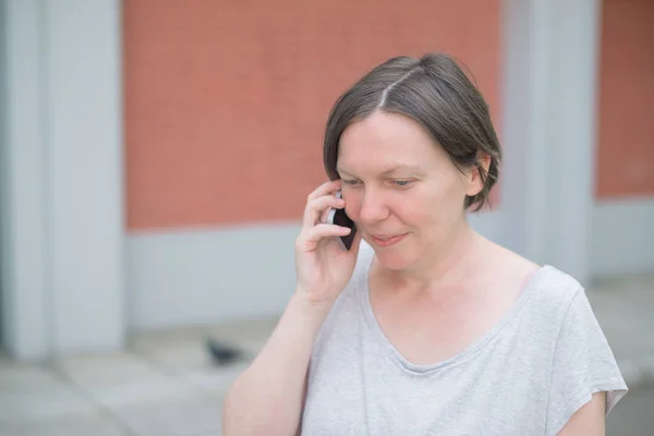 Улыбающаяся счастливая женщина разговаривает по мобильному телефону на улице — стоковое фото