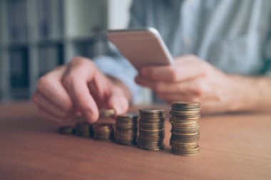 Ön planda yığılmış paralar ile Smartphone kullanarak iş adamı