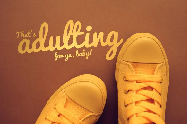 禧使用的词和词组 概念形象与年轻人在黄色运动鞋站立直接地在文本之上 Adulting — 图库照片