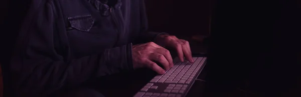 Computer hacker typing keyboard in dark interior, low key with selective focus