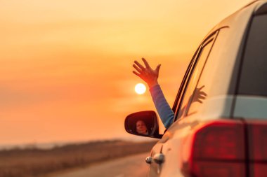 Sürücü kadın araba kullanırken elini pencereden dışarı çıkarıyor.