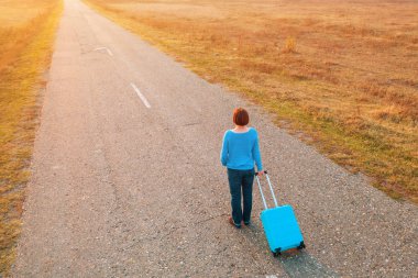 Sonbahar günbatımında seyahat valizlerini yolda taşıyan bir kadın.