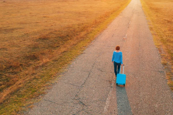 Woman pulling travel suitcase luggage on road in autumn sunset — Stock Photo, Image