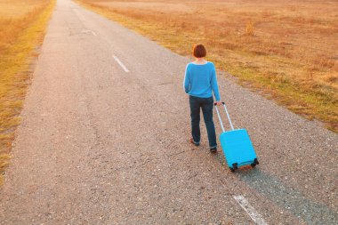 Sonbahar günbatımında seyahat valizlerini yolda taşıyan bir kadın.