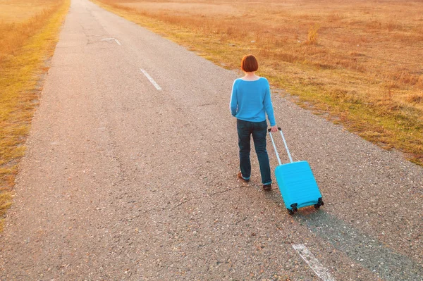 Sonbahar günbatımında seyahat valizlerini yolda taşıyan bir kadın. — Stok fotoğraf