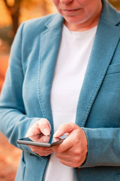 Donna d'affari digitando SMS sullo smartphone nel parco autunnale — Foto Stock