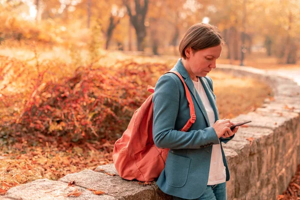 Podnikatelka pomocí mobilního telefonu v podzimním parku — Stock fotografie