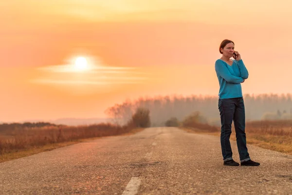Женщина, стоящая на сельской дороге и разговаривающая по мобильному телефону — стоковое фото