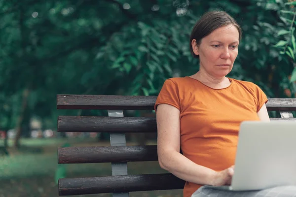 Woman using laptop computer on park bench — Stock Photo, Image