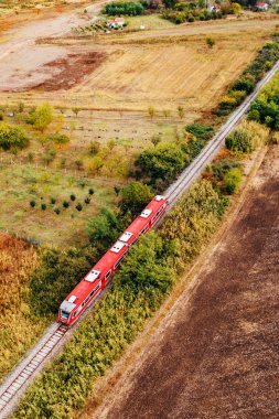 Kırmızı yolcu treni kırsal alanda ilerliyor, hava manzaralı.
