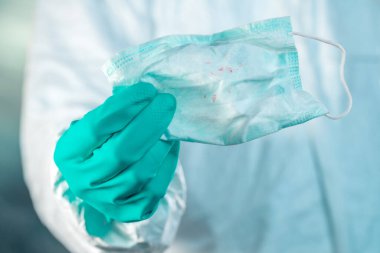 Epidemiyoloji uzmanı elinde kan lekeleriyle solunum maskesi tutuyor.