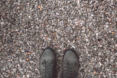 Standing on gravel stone ground, worn sneakers from above
