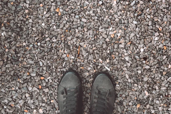 Standing on gravel stone ground, worn sneakers from above — Stockfoto