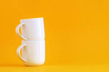 Sarı arkaplanda fotokopi alanı olan iki beyaz kahve fincanı.