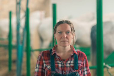 At ahırındaki kadın çiftlik sahibinin portresi kameraya bakıyor. Yetişkin kadın çiftlik işçisi olarak ekose gömlek ve kot önlük tulum giyiyor.