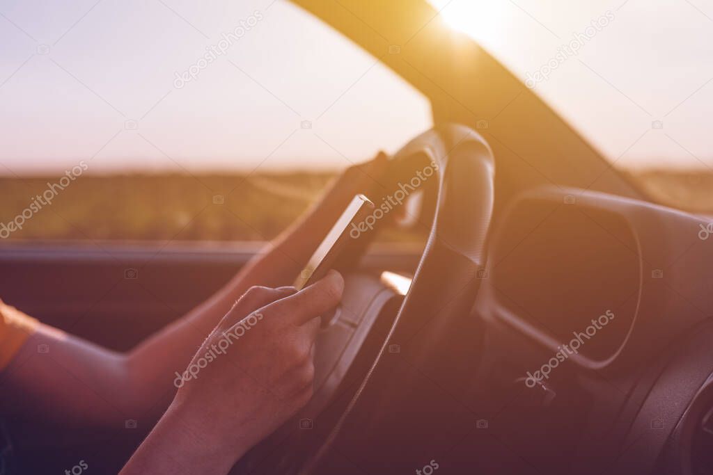 Dangerous texting while driving behavior, close up of female hands using mobile phone and operating motor vehicle on road through countryside, selective focus