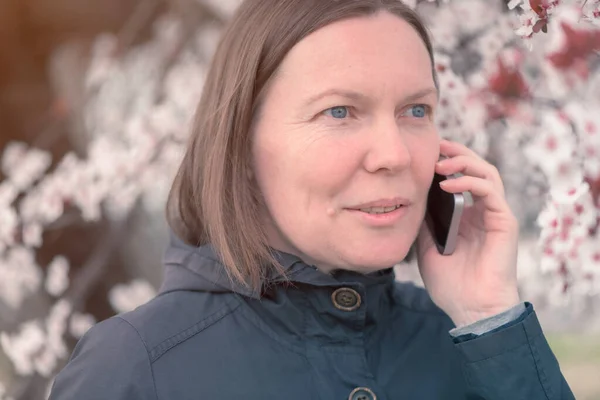 春の桜の下で携帯電話で話す深刻な女性 — ストック写真