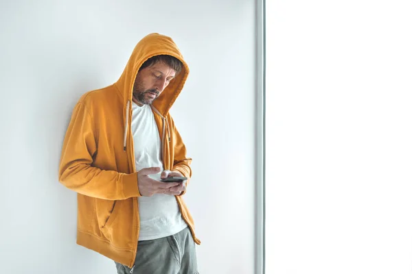 Mann Mit Gelbem Kapuzen Sweatshirt Mit Reißverschluss Nutzt Smartphone Fenster — Stockfoto