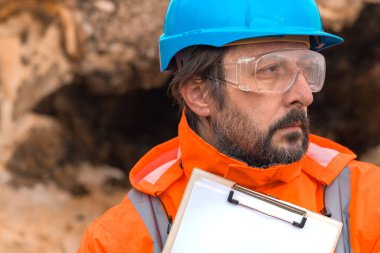 Ormandaki bir ağaç kütüğünün yanındaki not defteriyle poz veren orman teknisyeni, kendine güvenen profesyonel bir erkek sahada veri topluyor.