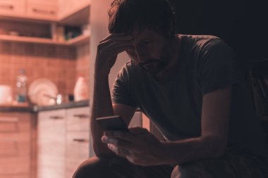 Karanlık odada cep telefonuna mesaj yazan depresif bir adam, seçici odaklanma