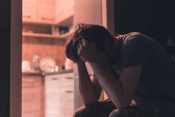 Депрессивный грустный мужчина плачет в темной комнате с головой в руках, избирательный фокус
