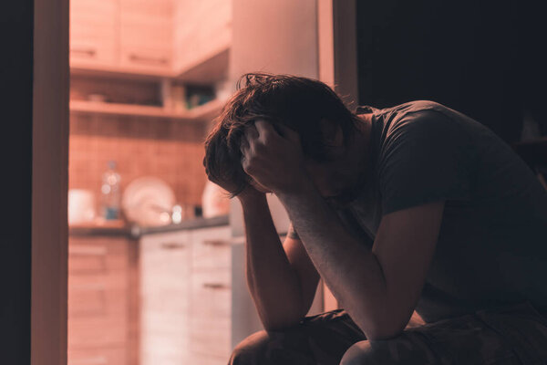 Depressed sad man crying in dark room with head in hands, selective focus