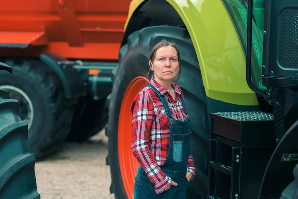 Female farmer and tractor. Woman doing men\'s job concept. Female farm worker posing in front of agricultural machinery.