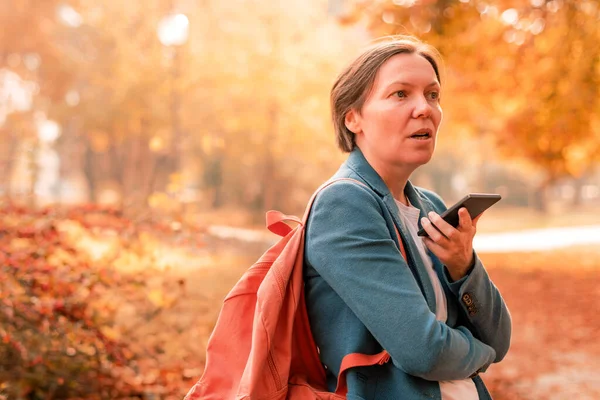在秋天的公园里 女商人用手机交谈 在她面前拿着智能手机 选择性地集中注意力 — 图库照片