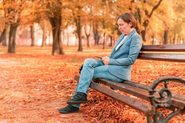 Vrouw Typt Tekst Mobiele Telefoon Herfstparkbank Kopieerruimte Met Selectieve Focus — Stockfoto