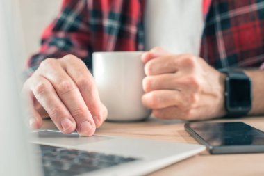 Laptop bilgisayarı kullanan ve ev içi ofiste kahve içen serbest çalışan, ellere özen gösteren biri.