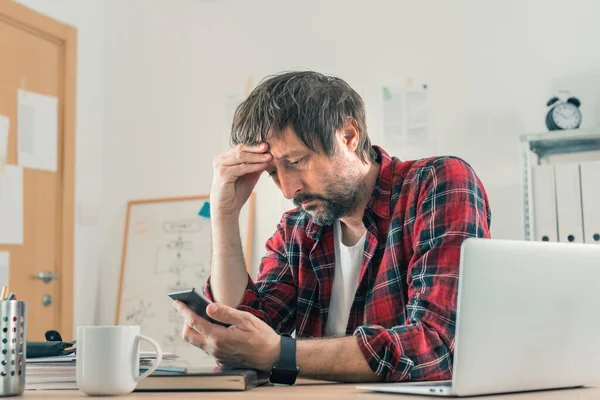 Freelancer Desapontado Problemático Usando Smartphone Para Comunicação Enquanto Sentado Mesa — Fotografia de Stock