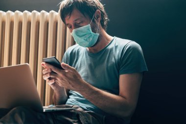 Virüs salgını sırasında evde dizüstü bilgisayar ve akıllı telefon kullanan bir adam kendini karantinada tutuyor.