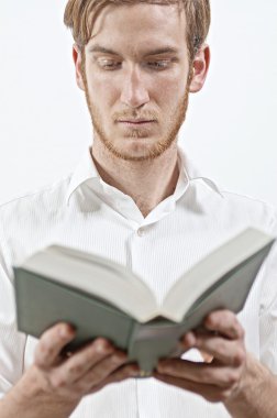 Beyaz gömlekli genç yetişkin adam ayakta bir kitap okuma elinde tutar