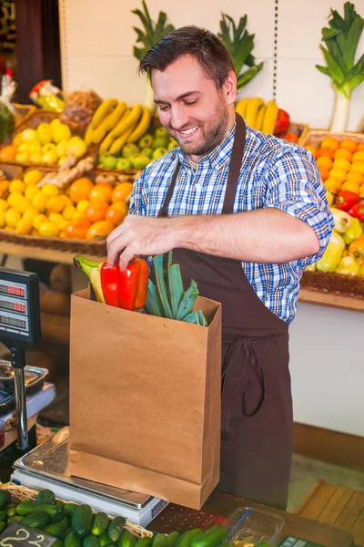 Seller in apron puts purchases in package — Stock Photo, Image