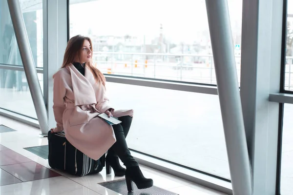 Mujer sentada en la maleta en la terminal del aeropuerto — Foto de Stock