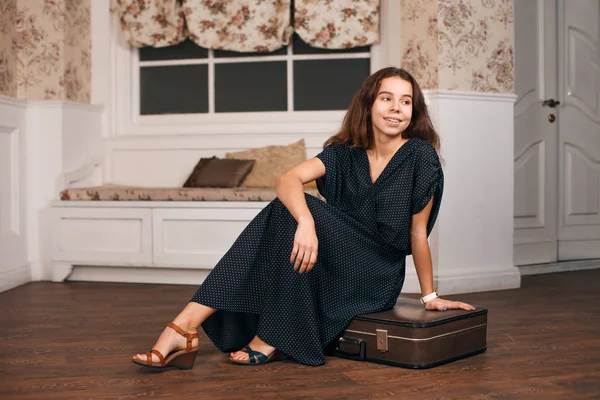 Woman in black dress sitting on suitcase — Stock Photo, Image