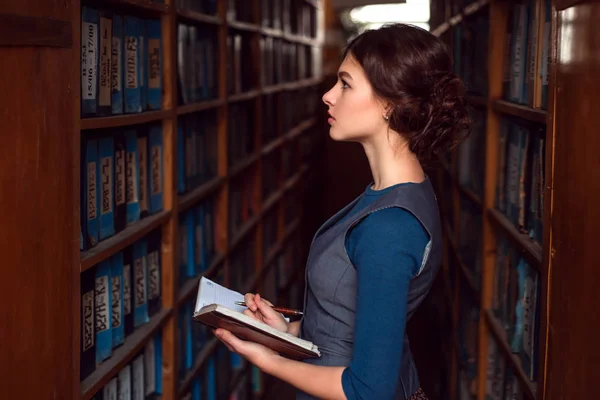 Giovane donna con quaderno in biblioteca — Foto Stock