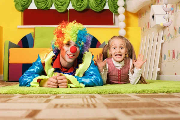 Liten flicka och clown liggande på matta — Stockfoto