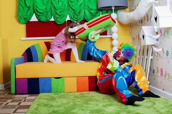 Little girl beating clown with pillow — Stock Photo, Image