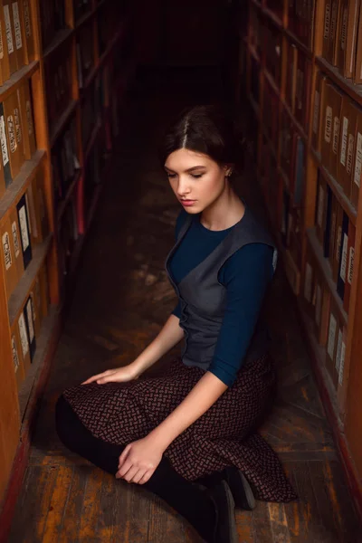 Молодая женщина сидит на полу в библиотеке — стоковое фото