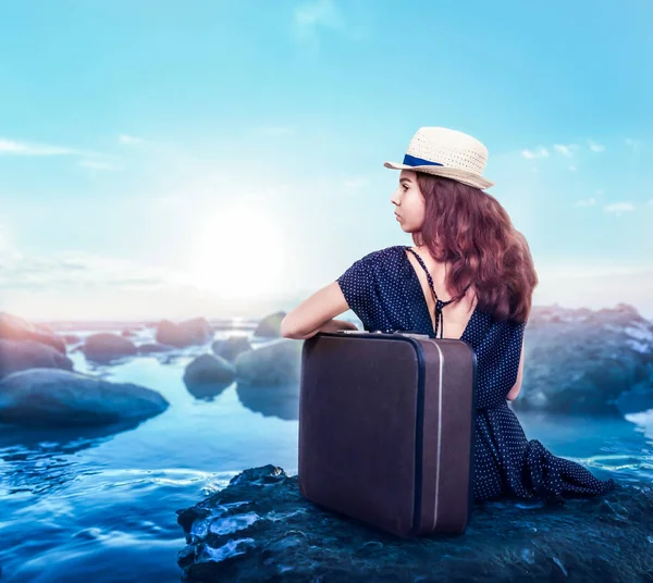 Молодая девушка с чемоданом сидит на камне . — стоковое фото