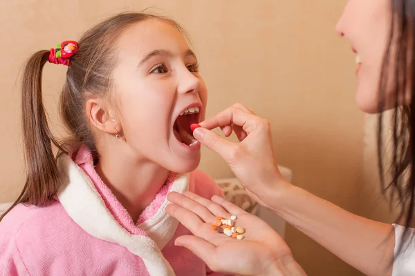 Mãe colocando comprimidos na boca da menina — Fotografia de Stock